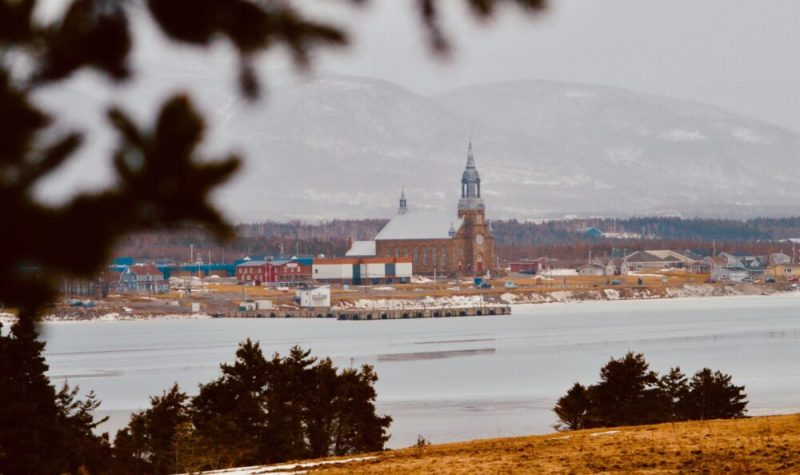 Église, école et maison au pieds des montagnes avec une baie en avant plan.