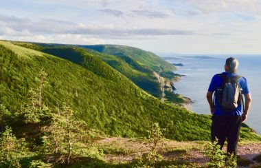 Un homme portant un chandail bleu, des culottes noires et une casquette au sommet d'une montagne.