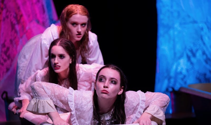 Three young women in white, old fashioned night gowns and pale makeup, appear to be climbing out of a bathtub.