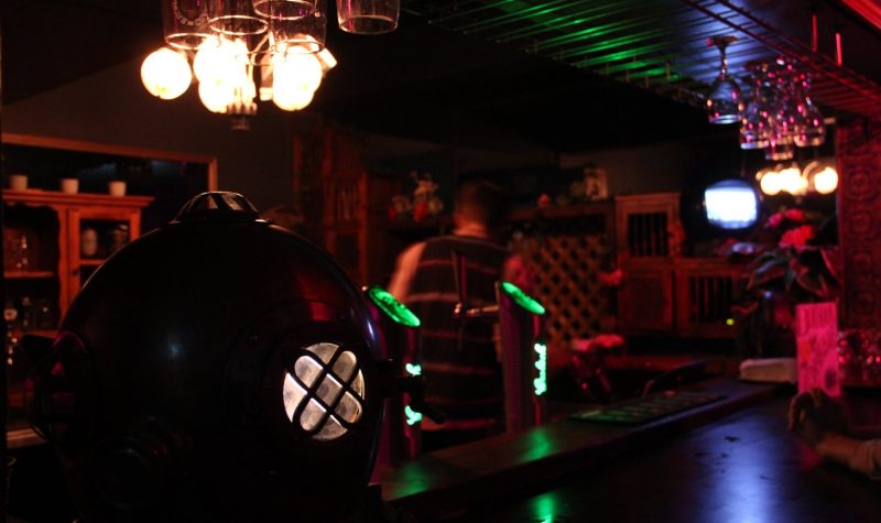 An old-timey diving helmet rests atop a dimly lit bar with multicoloured lights.