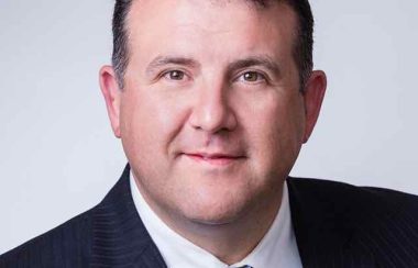 A head shot of a man in a suit and tie smiling at camera.