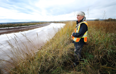 Woman is a fluorescent vest overlooking a tidal river.