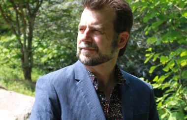 A headshot of David Gottfred standing in a wooded area wearing a blue sportcoat.