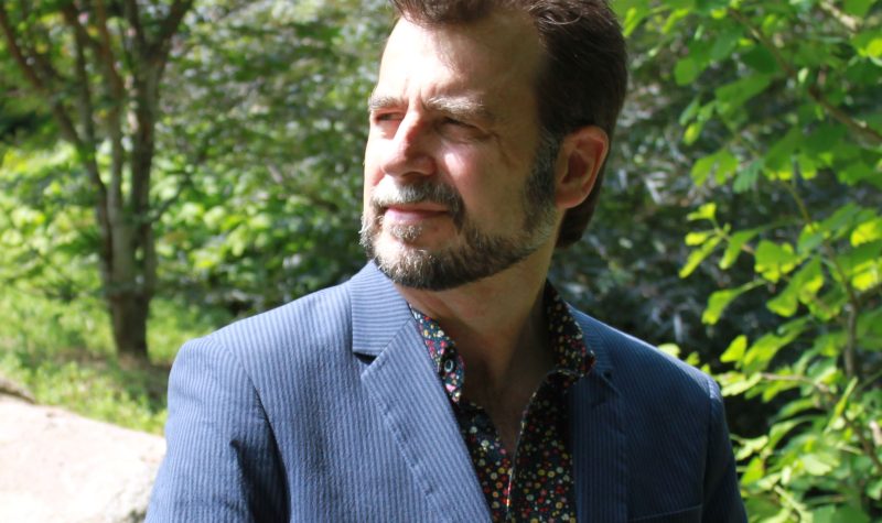 A headshot of David Gottfred standing in a wooded area wearing a blue sportcoat.