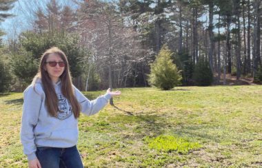 Woman stands in front of an empty field on a sunny day.