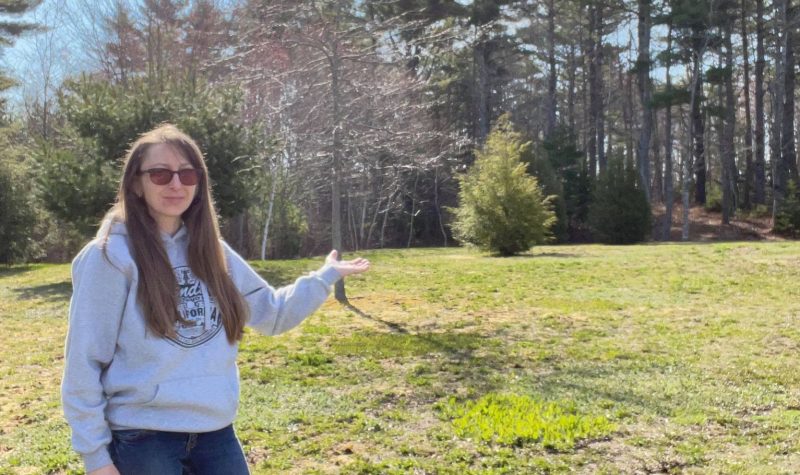 Woman stands in front of an empty field on a sunny day.