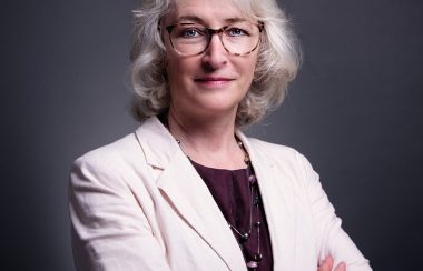 A progessional headshot of Denise Giroux wearing a white blazer and crossing her arms.