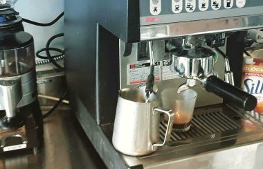 An espresso grinder and machine are next to one another, with a pitcher of milk rested under the steam wand.