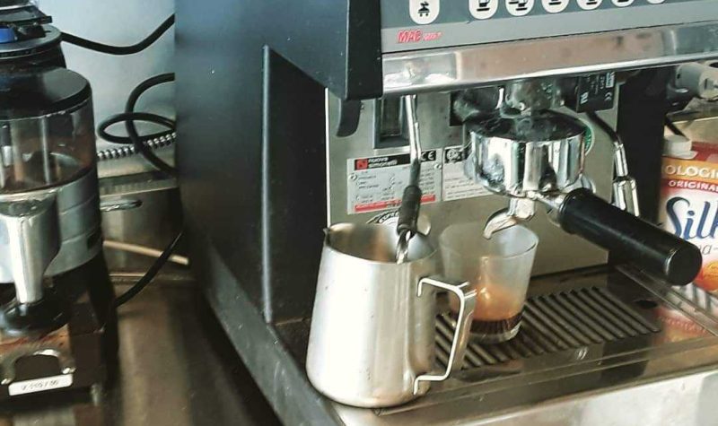 An espresso grinder and machine are next to one another, with a pitcher of milk rested under the steam wand.