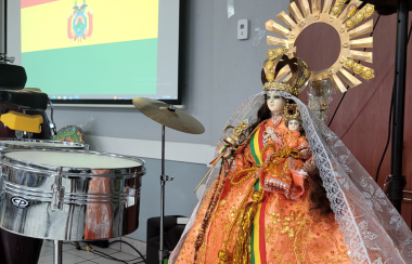 La imagen de una virgen en primer plano y detrás la bandera de Bolivia