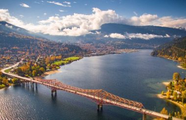 An aerial shot of Nelson BC on a sunny, summer day with Kootenay Lake and the Orange Bridge featured.