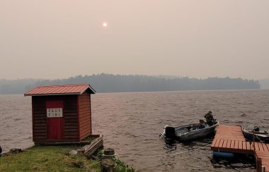 A photo of a dock and boat at a lake with the sky obscured by forest fire smoke.