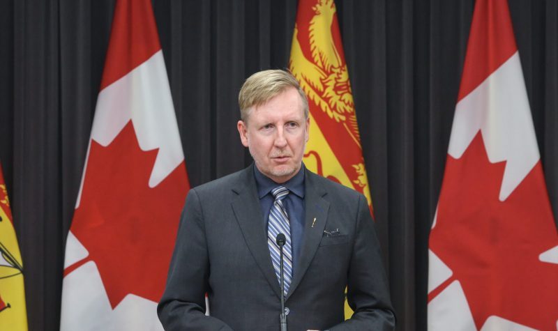 L'ancien ministre Dominic Cardy devant les drapeaux du Canada et du Nouveau-Brunswick.