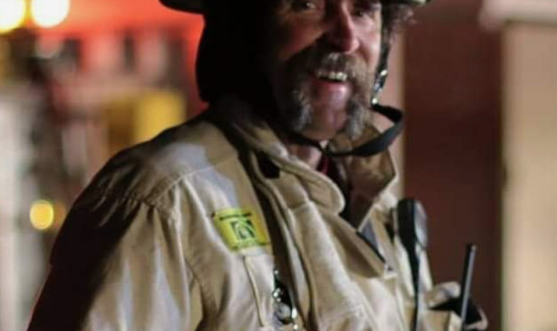A firefighter dressed in gear including helmet, coat and gloves, smiling.