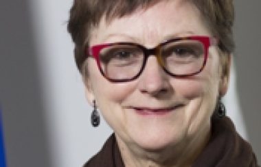 A professional headshot of Sheenboro Mayor Doris Ranger in front of a Quebec flag wearing a brown scarf and glasses.