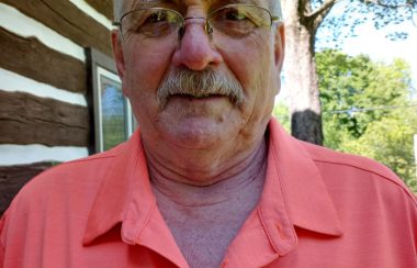 An outdoor selfie of Doug Rousselle, wearing glasses and an orange golf shirt.