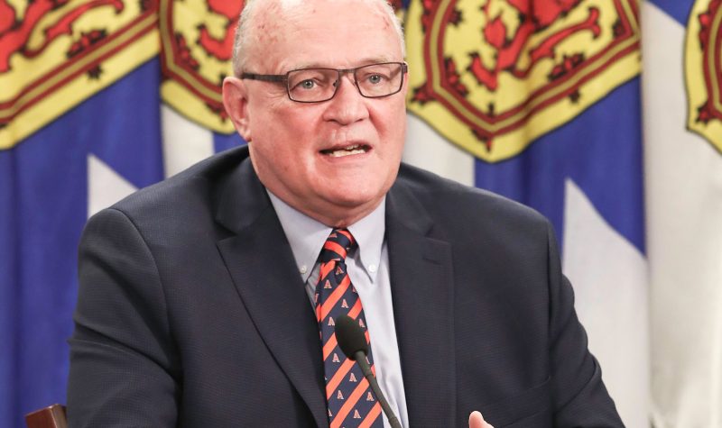 A close up of Dr. Robert Strang speaking at a podium with Nova Scotia flags behind him.