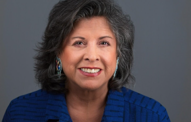 A woman in a blue shirt sitting against a dark grey background