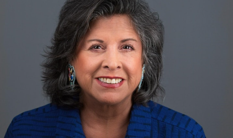 A woman in a blue shirt sitting against a dark grey background