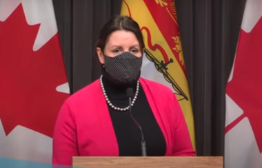 Dr. Jennifer Russell wears a mask and stands behind a podium.
