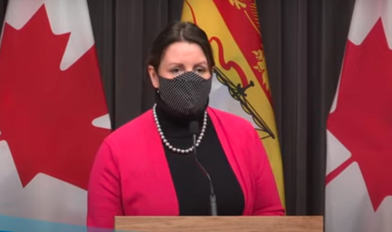 Dr. Jennifer Russell wears a mask and stands behind a podium.