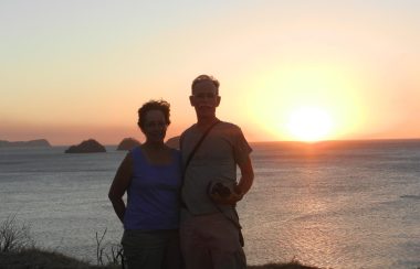 Dr. Maurice Lamarche and his wife France standing in front of a body of water at sunset.