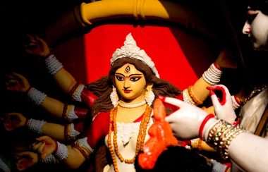 A girl with fingernails painted red touches a statue of the Hindu goddess Durga