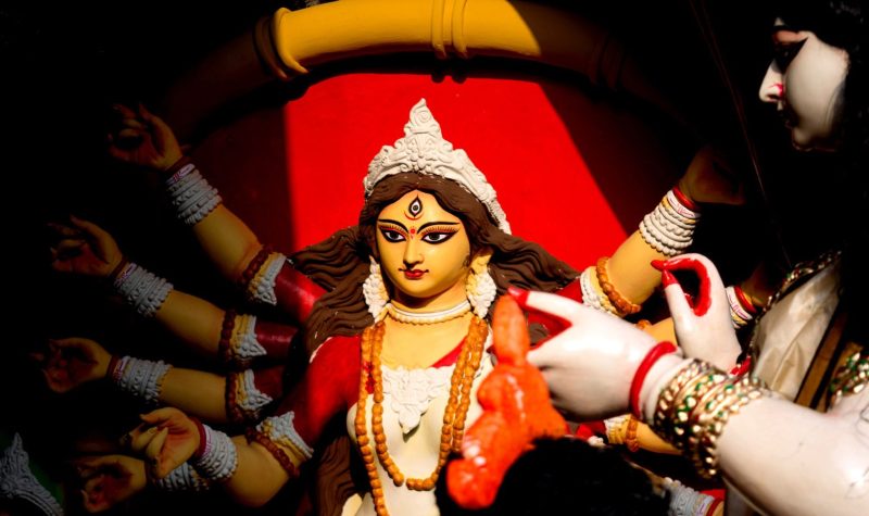 A girl with fingernails painted red touches a statue of the Hindu goddess Durga