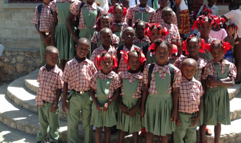 Des jeunes du primaire en uniforme, chemise à carreaux rouge et blanc , pantalon vert pour les garçons et jupe verte pour les filles et leur ruban rouge.