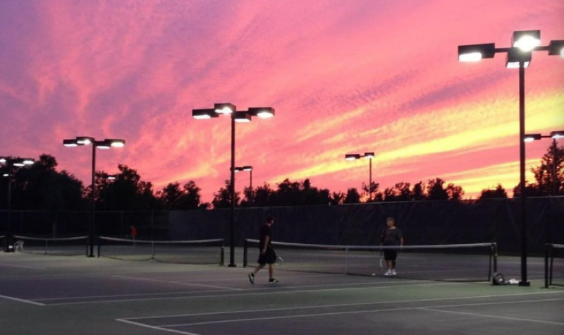 A pink/orange sunset sky is over top of tennis courts.