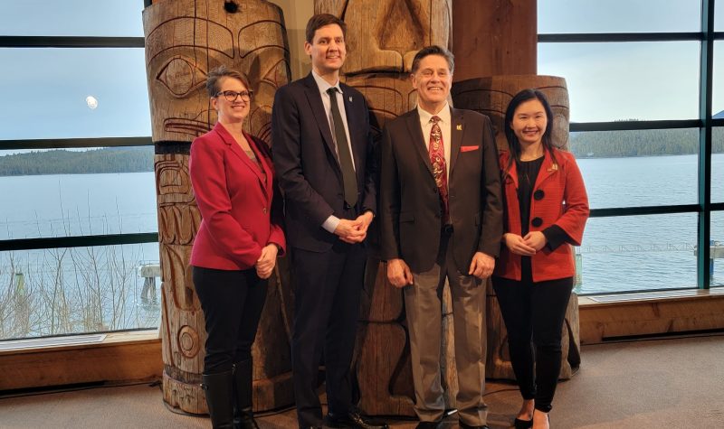 4 people stand in front of traditional indigenous carvings