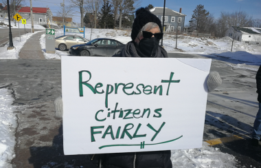 A woman outside in winter holding a sign that says, 