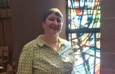 Woman standing in front of stained glass window.