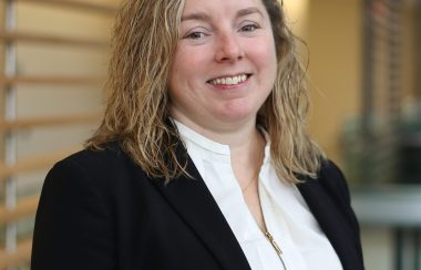 A woman stands in front of a blurred office background