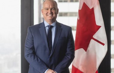 A man stands beside a Canadian flag