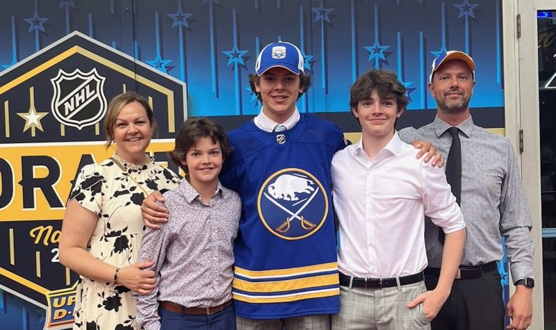 Ethan Miedema and family pose for a picture at the NHL draft. There is a blue background behind the five people.
