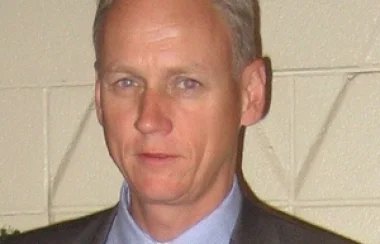 A man stands in front of a wall wearing a suit and tie