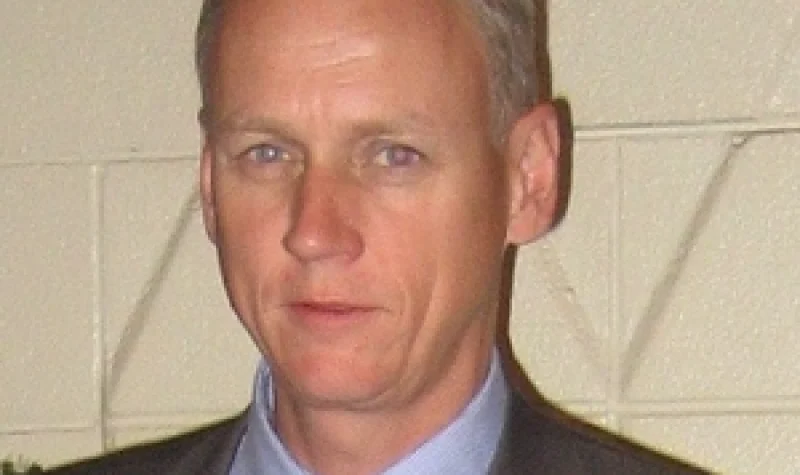 A man stands in front of a wall wearing a suit and tie