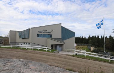 Le bâtiment de l'école Gabriel-Dionne, gris et bleu, avec un drapeau du Québec flottant à ses côtés.