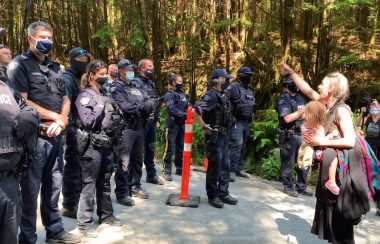 A woman with a child shouts at a line of RCMP officers near the Fairy Creek Blockades