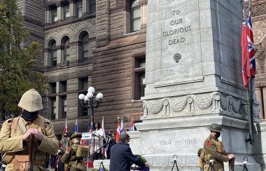 A man places a wreath on a stand infront a large statue.