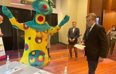 A person in a colourful animal-like coustume beside a man in a black suit.