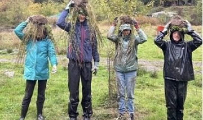 Four youth standing in a row with native plants balanced on their heads at the Dillon Creek Wetlands