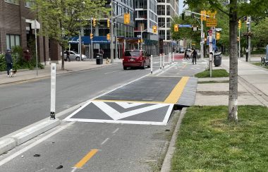 A two-way bike lane with white and yellow lines beside a patch on grass in a city setting.