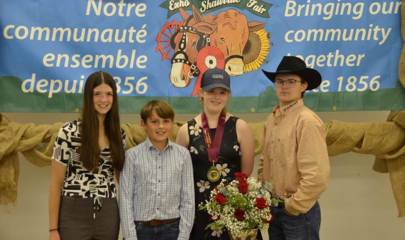Four youths stand in front of a poster for the Shawville Fair.