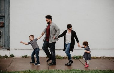Une famille de 4 marche main dans la main sur un trottoir légèrement mouillé