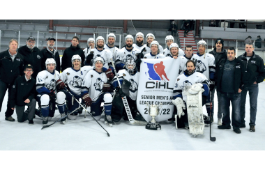 A team of hockey players in their uniforms holding a championship banner on the ice with their coaches who are dressed in black.