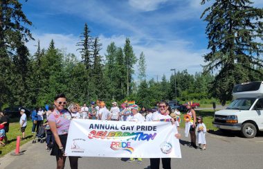 Two people hold a banner saying Annual Gay Pride Celebration in front of a large crowd