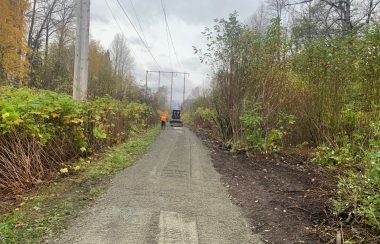 A person with a high visibility vest in front of a small front end loader vehicle laying gravel