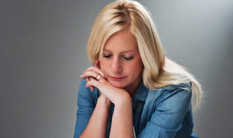Une femme blonde attristé avec une chemise jeans avec des manches retroussées